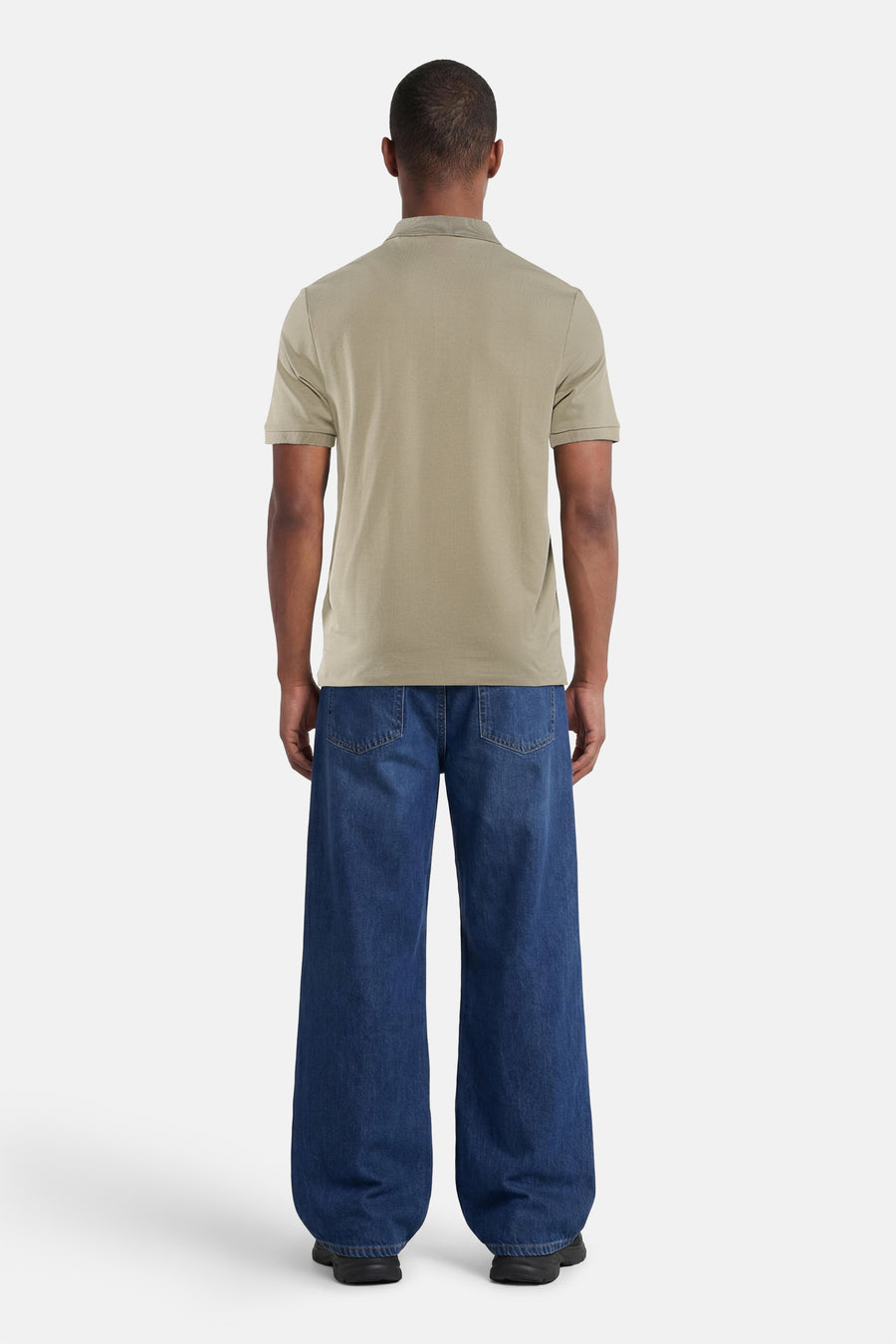 Polo verte HUGO, vue de dos par un homme, combinée avec un jean ample et des baskets.