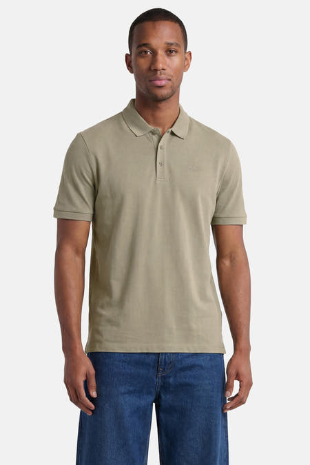 Groene polo van HUGO met twee knopen, een geborduurd logo, gedragen door een man in een spijkerbroek.