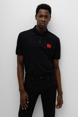 Zwarte polo van HUGO met korte mouwen en een rood logo, gedragen met een zwarte jeans.
