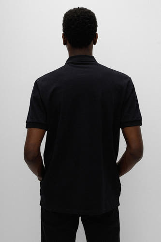 Zwarte polo van HUGO, achterkant gezien, met korte mouwen en de handen in de zakken.