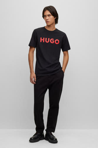 T-shirt noir à manches courtes de HUGO, avec le nom de marque rouge sur la poitrine, associé à un pantalon noir et des chaussures.
