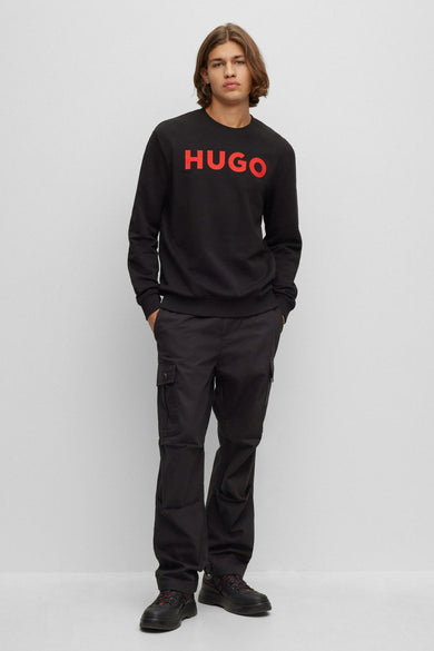 Zwarte sweater met ronde hals van HUGO, met rode merklogo op de voorkant, gecombineerd met zwarte cargobroek en schoenen.