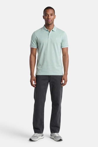 Turquoise polo van HUGO BOSS ORANGE met witte bies op kraag en mouwen, gedragen door een man met donkere broek en grijze sneakers.