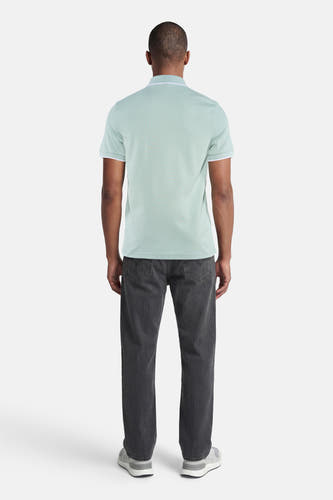 Turquoise polo van HUGO BOSS ORANGE met witte bies aan kraag en mouwen, achterzijde op man met donkere jeans en grijze sneakers.
