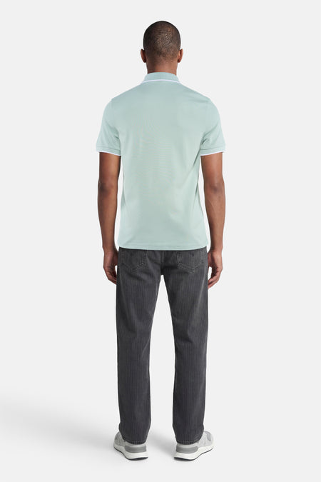 Turquoise polo van HUGO BOSS ORANGE met witte bies aan kraag en mouwen, achterzijde op man met donkere jeans en grijze sneakers.