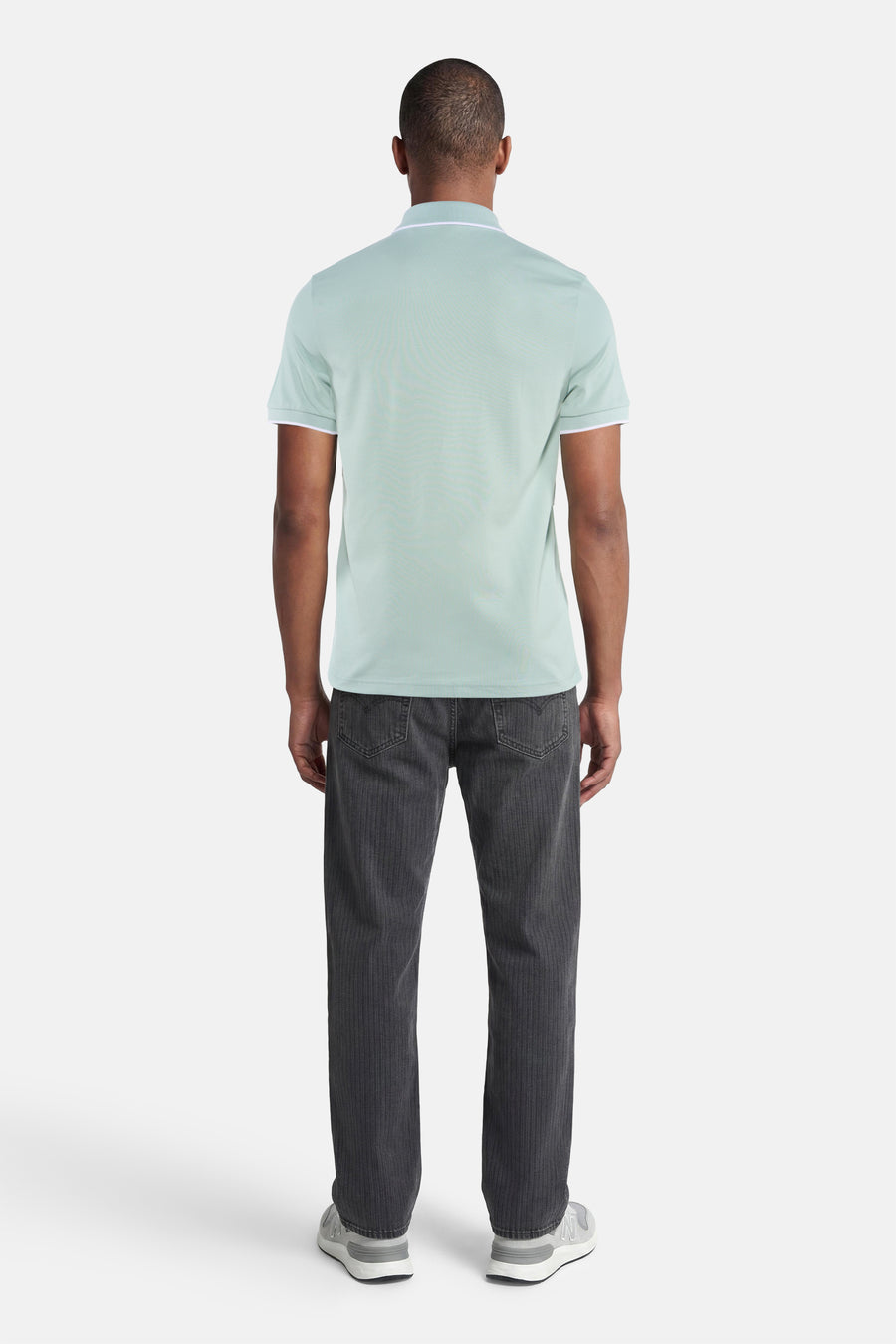 Turquoise polo van HUGO BOSS ORANGE met witte bies aan kraag en mouwen, achterzijde op man met donkere jeans en grijze sneakers.