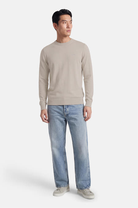 Grijze trui met ronde hals van HUGO BOSS ORANGE, gedragen met blauwe jeans en suède sneakers.

