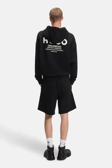 Pull-over noir avec capuche de HUGO BLUE, avec impression de logo blanc sur le dos, associé à un short et des chaussures.