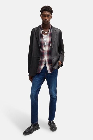 Tapered jeans van midblauw denim van HUGO, gecombineerd met een overhemd met ruitpatroon, een zwart jasje en zwarte schoenen.