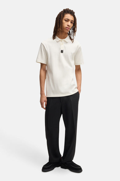 Man met dreadlocks, witte polo, zwarte broek en schoenen.