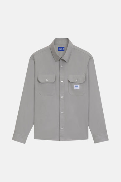 Chemise grise à manches longues de HUGO BLUE, avec deux poches po poitrine et col boutonné, sur un fond blanc.
