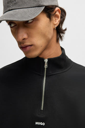 Zwarte sweater met rits van HUGO, gedragen met een grijze pet met logo.