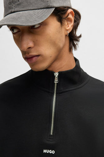 Zwarte sweater met rits van HUGO, gedragen met een grijze pet met logo.