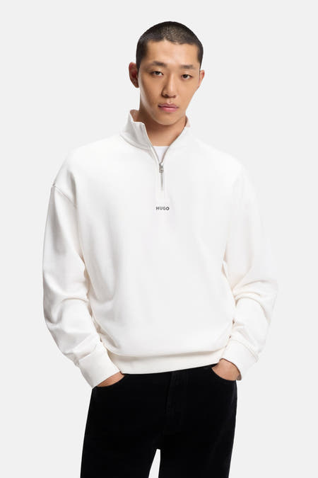 Witte sweater met korte rits van HUGO, gedragen met zwarte broek met zakken.
