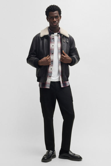 Rood, lange mouwen overhemd van HUGO, gedragen over een wit T-shirt, met daarover een zwarte pilotenjas met een witte kraag.