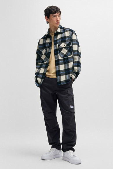 Zwart overhemd met lange mouwen van HUGO BLUE, met een geruit patroon en gedragen over een bruin T-shirt, met zwarte broek en witte sneakers.