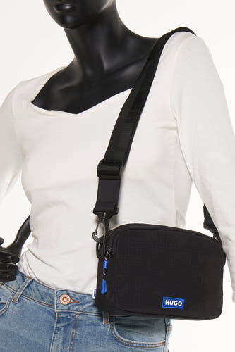 Zwarte schoudertas van HUGO BLUE, met verstelbare band en blauwe accenten, gedragen door een mannequin met jeans en wit shirt.
