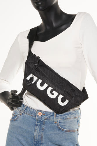 Zwarte schoudertas van HUGO met een textuur en een wit HUGO logo, gedragen met een wit shirt en een blauwe jeans.
