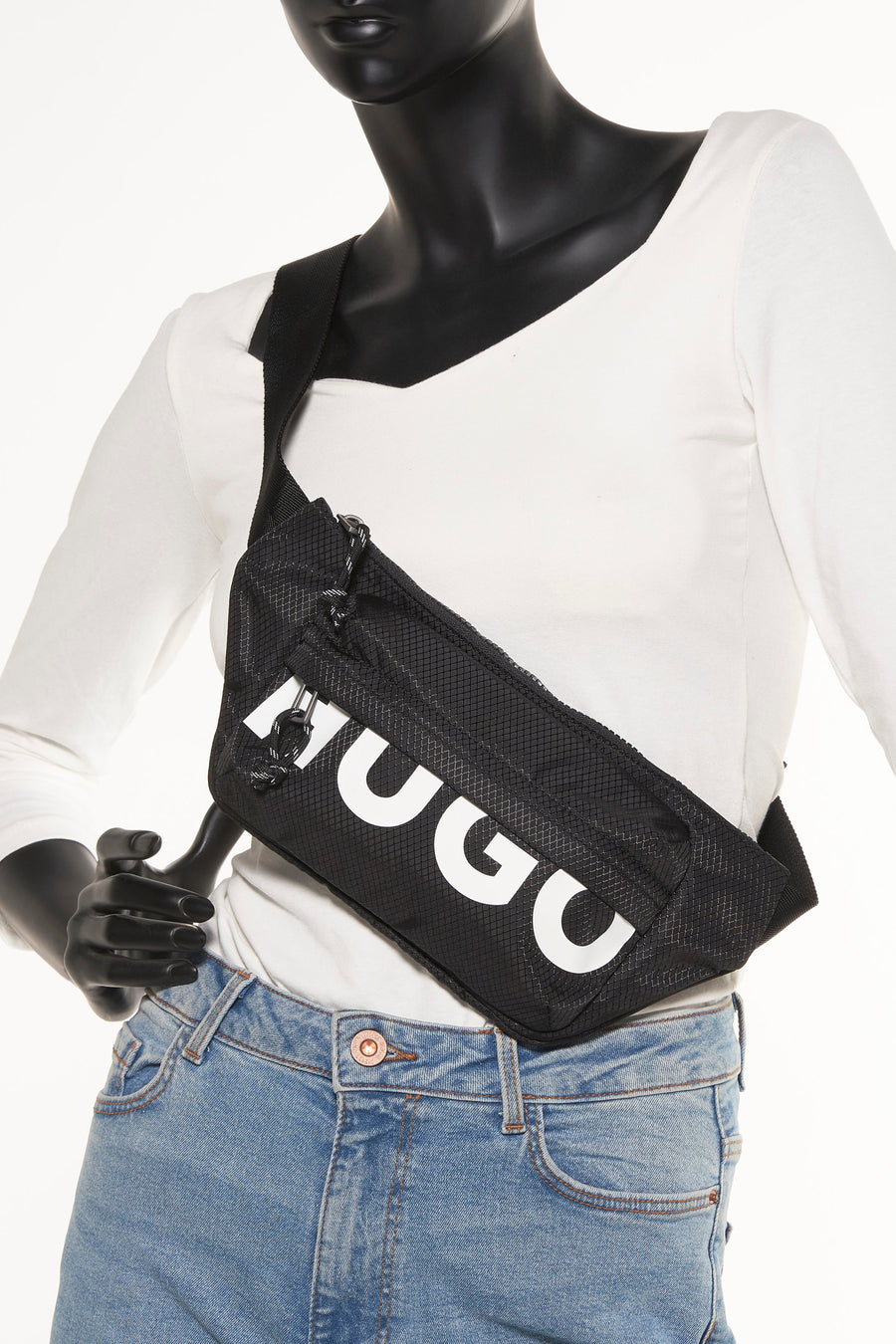 Zwarte schoudertas van HUGO met een textuur en een wit HUGO logo, gedragen met een wit shirt en een blauwe jeans.
