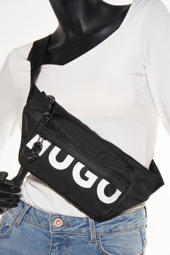 Zwarte schoudertas van HUGO, met een ruitjespatroon en witte merkletters, gedragen over een witte top en een jeans.
