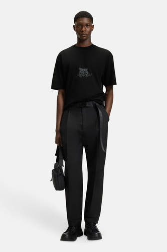 T-shirt noir à manches courtes de HUGO, avec une subtile impression et associé à un pantalon noir et un sac crossbody.