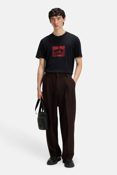 T-shirt noir à manches courtes de HUGO, avec un imprimé de lèvres rouges sur l'avant, associé à un pantalon marron et une sac noir.