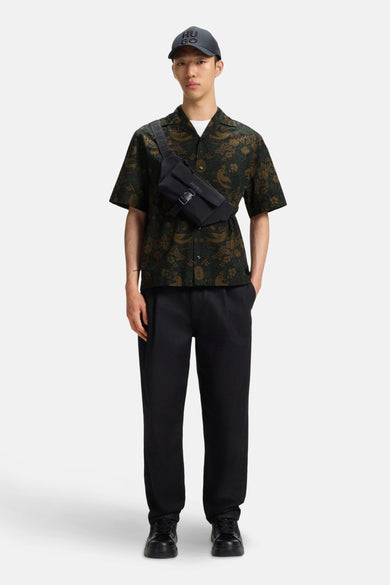 Chemise verte à manches courtes de HUGO, avec un motif d'oiseau botanique et portée avec une ceinture noire.
