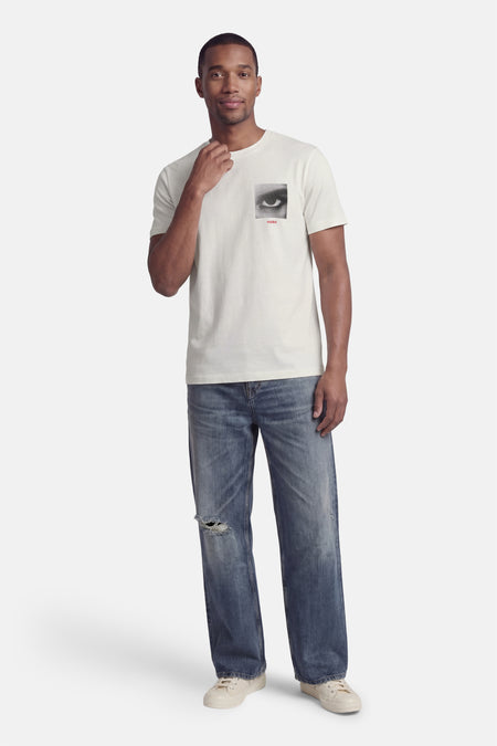 Wit T-shirt met korte mouwen van HUGO, met een zwart-wit oog print op de borst, gedragen met jeans met scheuren.
