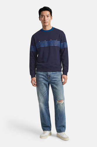 Donkerblauwe ronde hals sweater van HUGO met blauwe strepen en logo, gedragen met gescheurde jeans en witte sneakers, front view