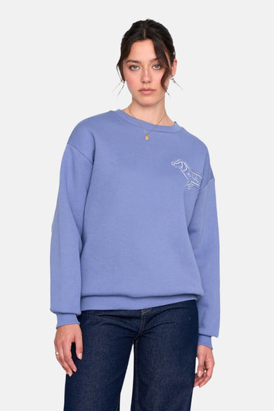 Blauwe sweater met ronde hals van 24 colours gmbh, met geborduurde hond, gedragen met donkere jeans en gouden ketting.
