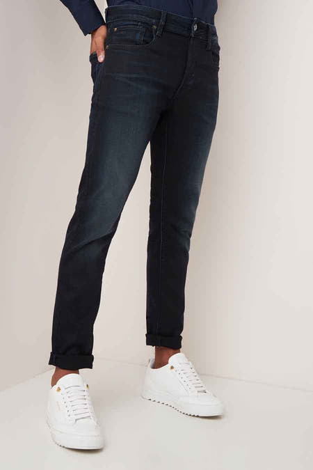 Donkerblauwe slim jeans van G-Star RAW, met omgeslagen pijpen en gecombineerd met witte sneakers.
