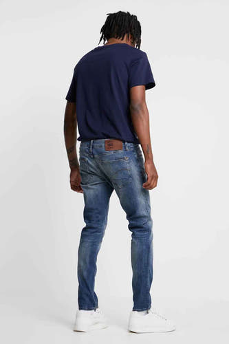 Slim jeans van middenblauw denim van G-Star RAW, gezien van achteren, met witte sneakers.