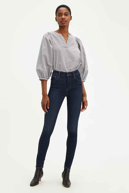 Donkerblauwe skinny jeans van Levi's, gedragen met een zwart-wit geruite blouse en zwarte enkellaarsjes.
