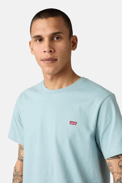 Blauw T-shirt met korte mouwen van Levi's, met klein rood logo op de borst en tatoeages zichtbaar op de armen.
