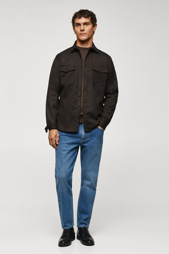 Chemise brune à manches longues de MANGO, avec poches sur la poitrine, associée à une veste brune et des jeans bleus.