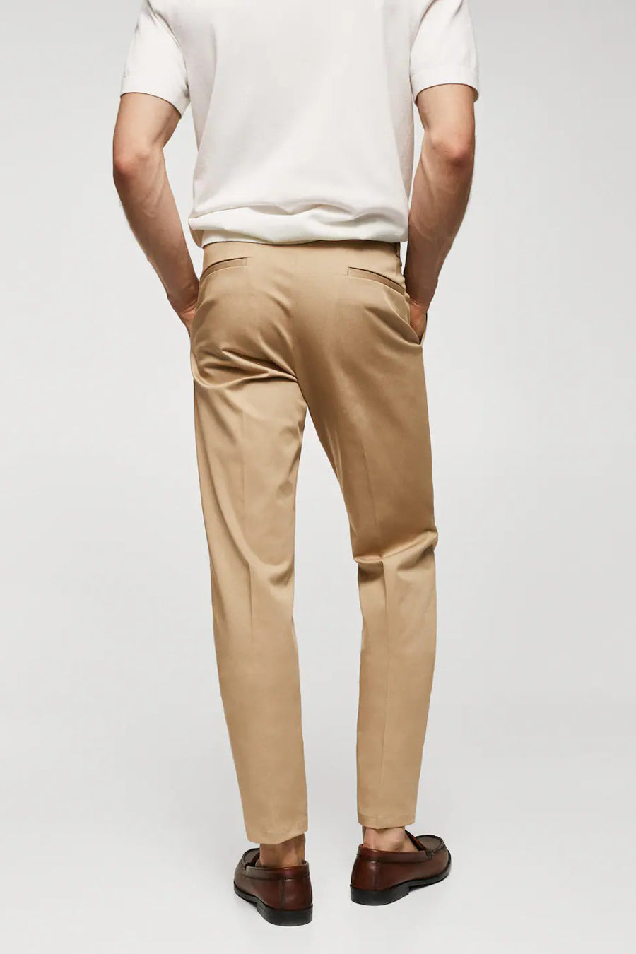 Bruine chino van MANGO, gezien van achteren, gecombineerd met een wit shirt en bruine instappers.

