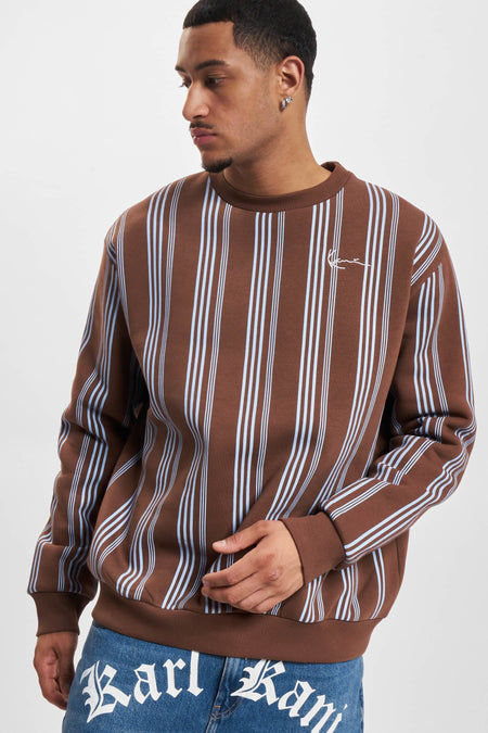 Bruine sweater met ronde hals van Karl Kani, met verticale blauwe strepen en denim broek zichtbaar.
