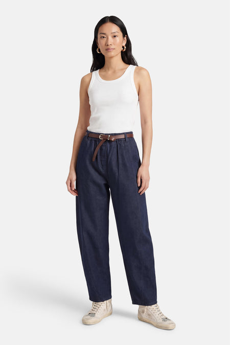 Mom jeans van donkerblauw denim van Terra di Siena, met een bruine riem, gecombineerd met een wit hemdje en crèmekleurige sneakers.