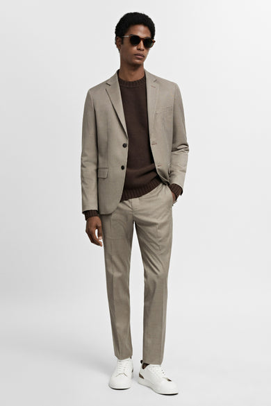 Beige kostuumbroek van MANGO, gecombineerd met een bruine trui, colbert en witte sneakers.