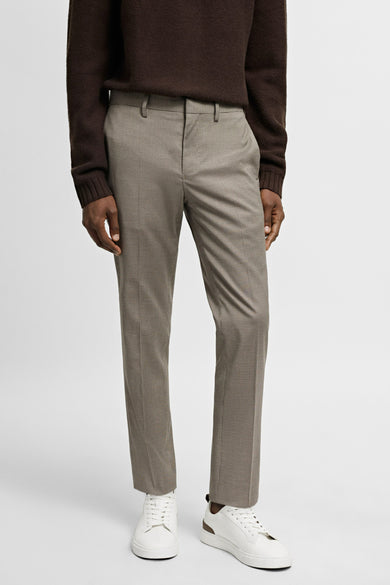 Beige kostuumbroek van MANGO, met een subtiel ruitpatroon, gecombineerd met een bruine trui en witte sneakers.
