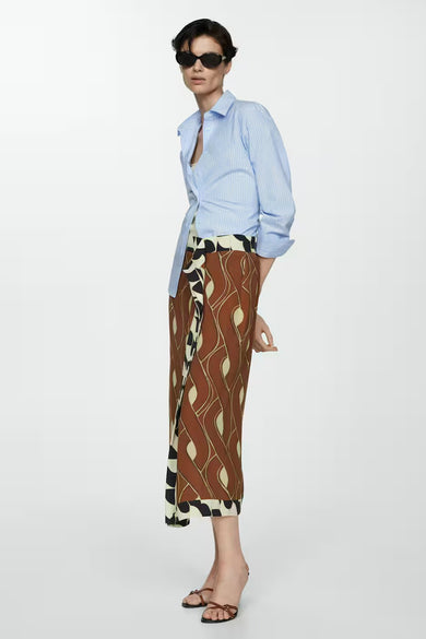 Jupe brune de MANGO avec un motif frappant, associée à une chemise rayée bleue et des sandales.