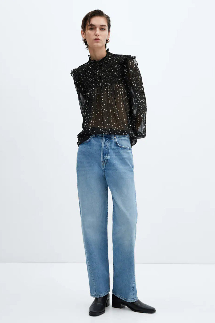 Blouse noire à manches longues de MANGO, avec un motif à points, associée à des jeans bleus et des bottes noires.