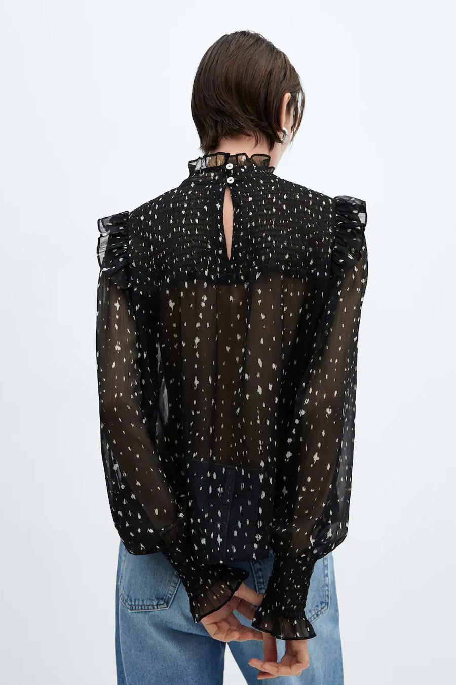 Blouse noire de MANGO avec des manches longues, un motif à carreaux, des volants sur les épaules et un détail plié.