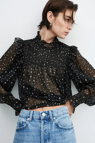 Blouse noire de MANGO à longues manches et à petits points blancs, associée à un jean.