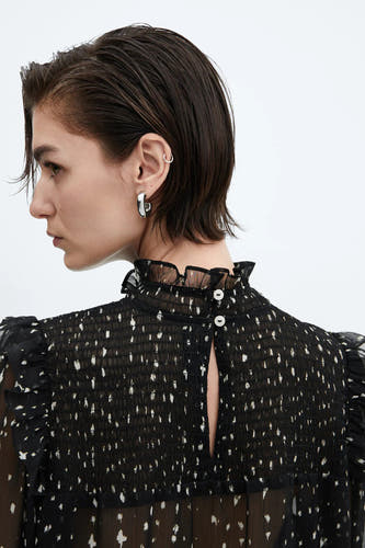 Blouse noire à manches longues de MANGO, avec des taches blanches, des détails plissés et une fermeture à boutons à l'arrière.