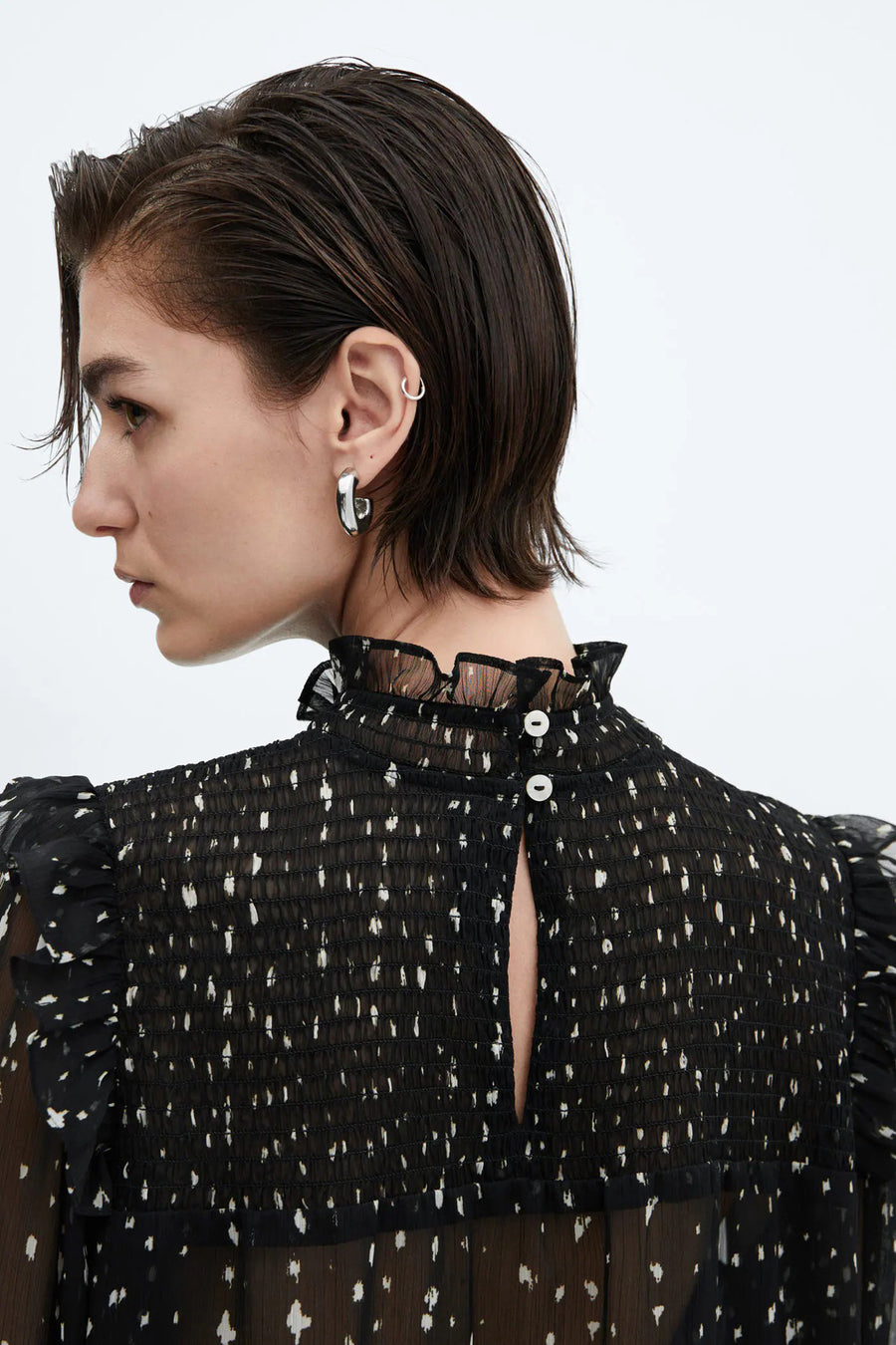 Blouse noire à manches longues de MANGO, avec des taches blanches, des détails plissés et une fermeture à boutons à l'arrière.