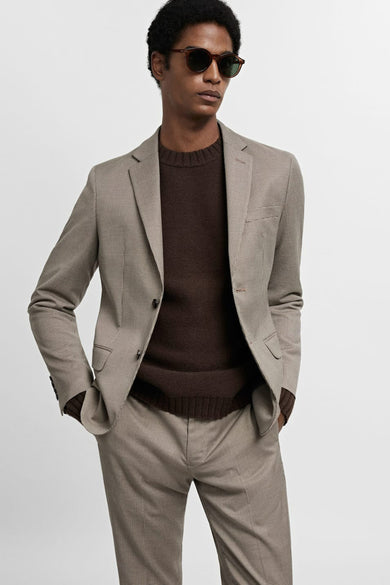 Beige blazer van MANGO, met een subtiel geruit patroon, gecombineerd met een bruine trui en zonnebril.