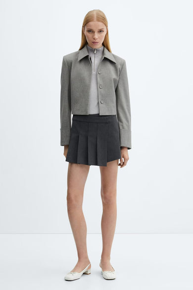 Pull en argent avec col rond de MANGO, porté sous une veste grise et une jupe plissée coordonnée.