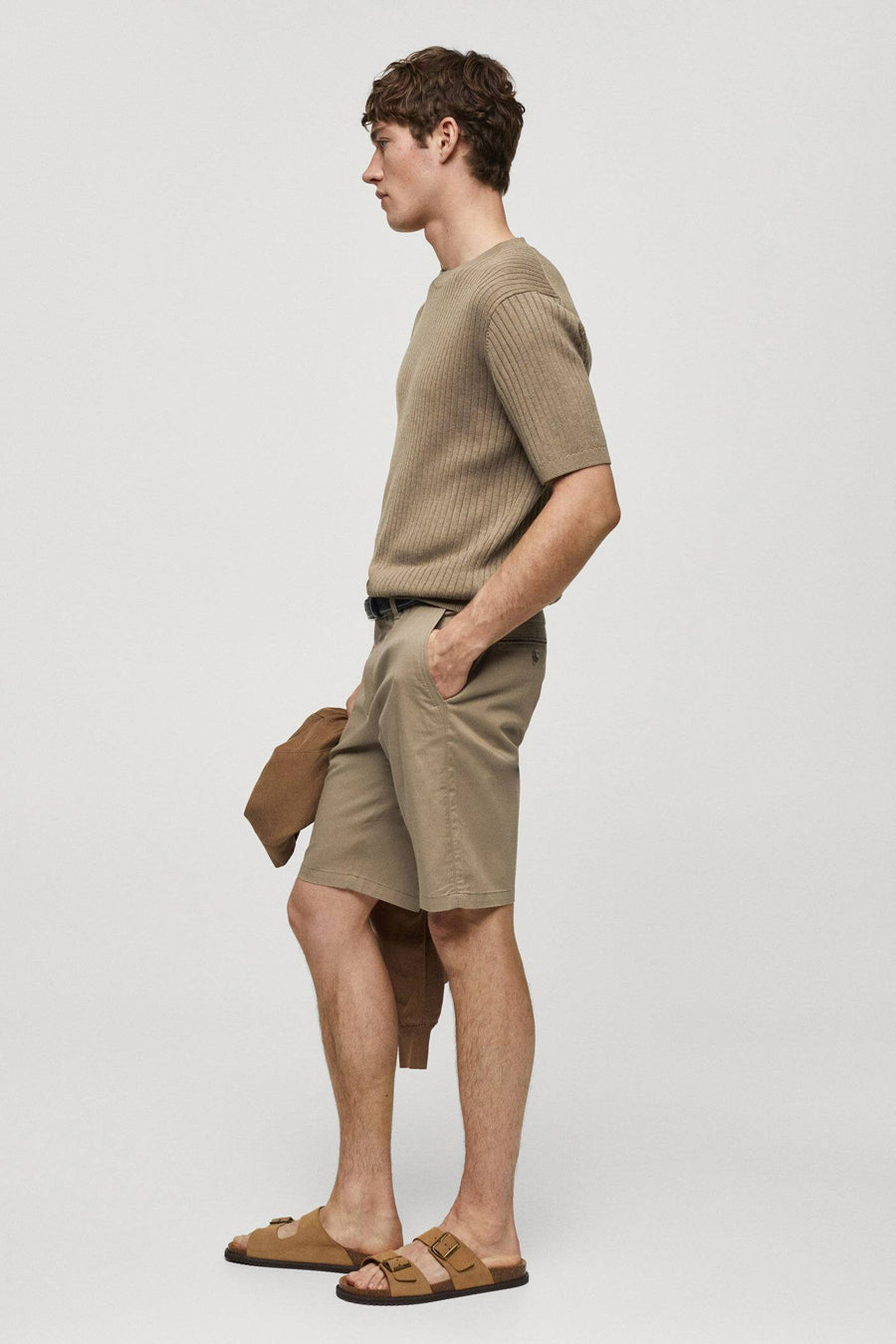 Bruine short van MANGO, met een riem en een bijpassende jas in de hand, gezien in zijaanzicht.
