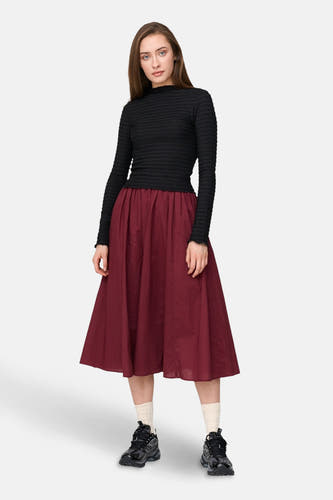 Bordeaux rok van 24 colours gmbh, met een uitlopende vorm, gecombineerd met een zwarte top en sportschoenen.
